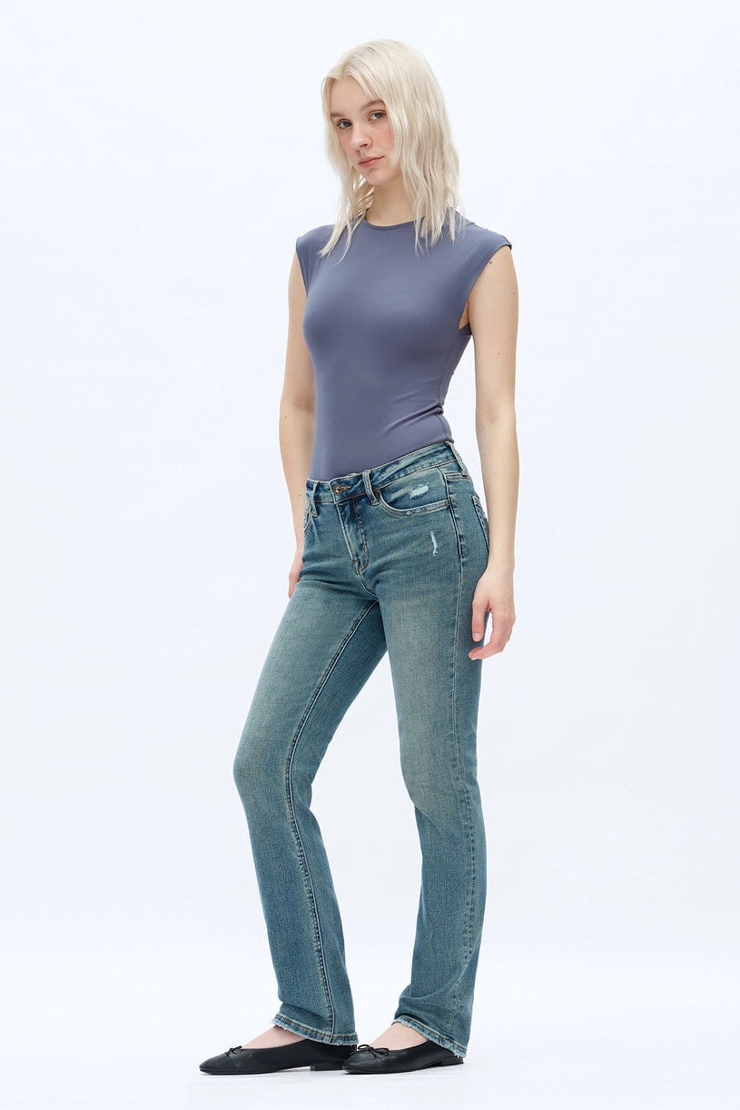 A person wearing dark blue straight-leg  bootcut jeans with a light yellow top and brown sandals, shown from the waist down against a plain white studio background.