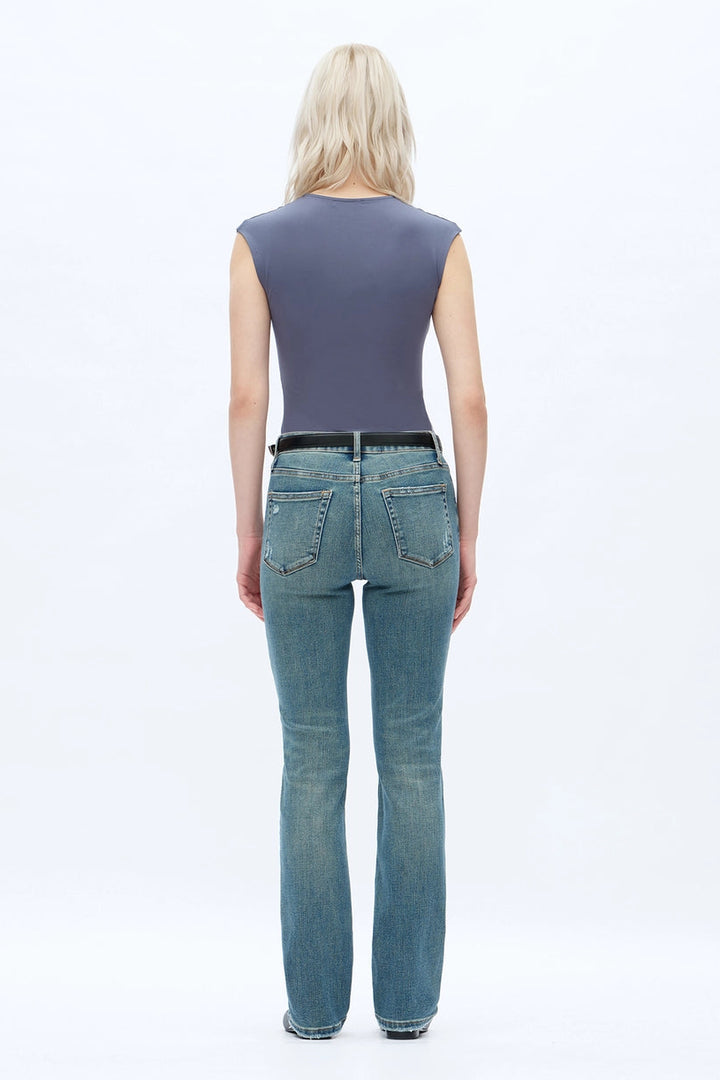 A person wearing dark blue straight-leg  bootcut jeans with a light yellow top and brown sandals, shown from the waist down against a plain white studio background.