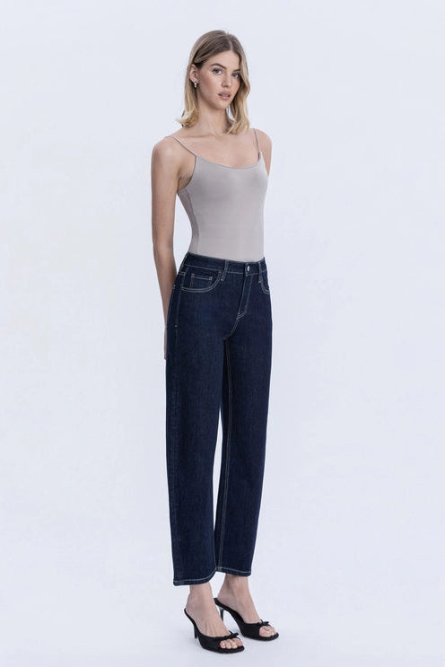 A woman modeling dark wash wide-leg cropped jeans with a light gray camisole top and black heeled sandals, standing against a plain white studio background.