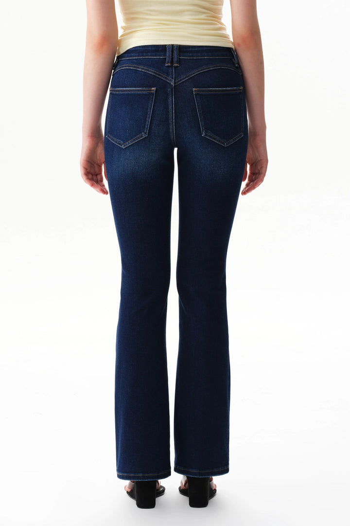 A person wearing dark blue straight-leg  bootcut jeans with a light yellow top and brown sandals, shown from the waist down against a plain white studio background.