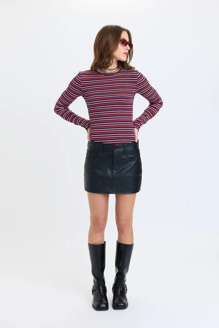 A model stands against a plain white studio background wearing a long-sleeve striped knit top with red, navy, and white horizontal stripes, a coated black daze fever micro mini skirt, and black knee-high boots.