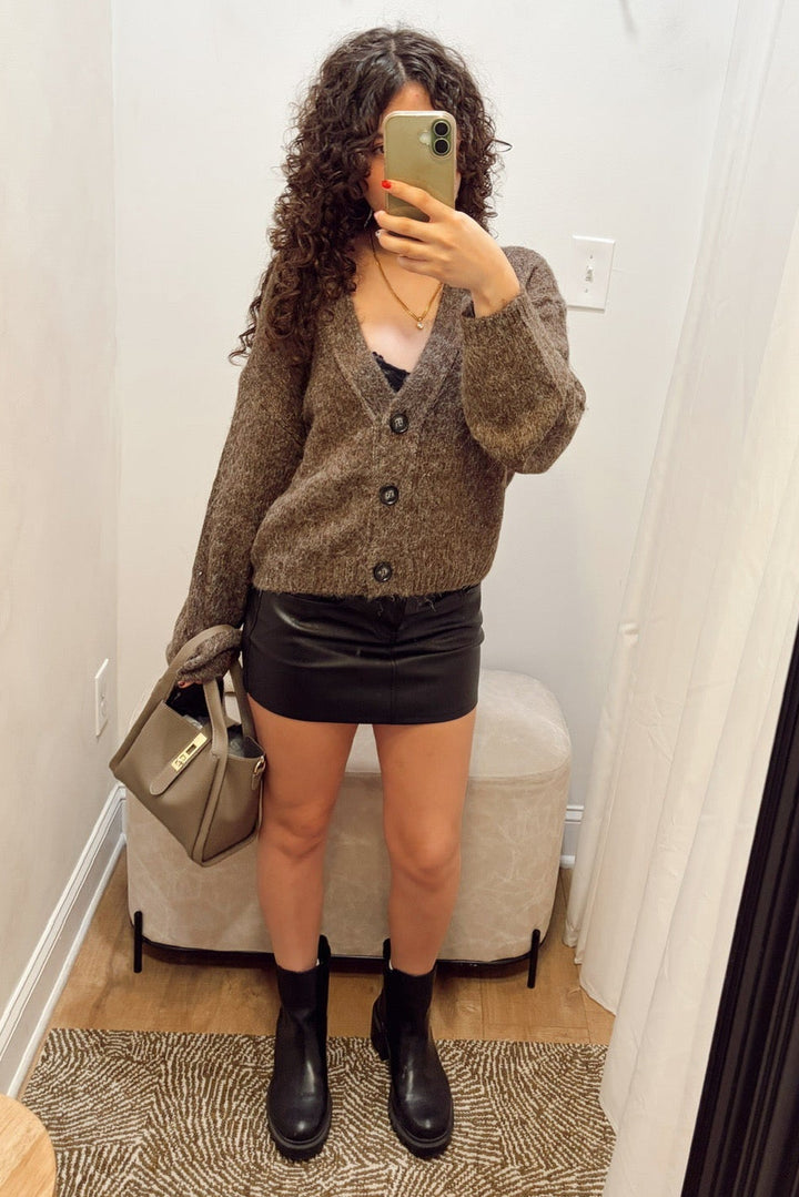  brown steve madden mica fuzzy knit cardigan with black buttons, a black daze denim leather mini skirt, and holding a taupe tote bag