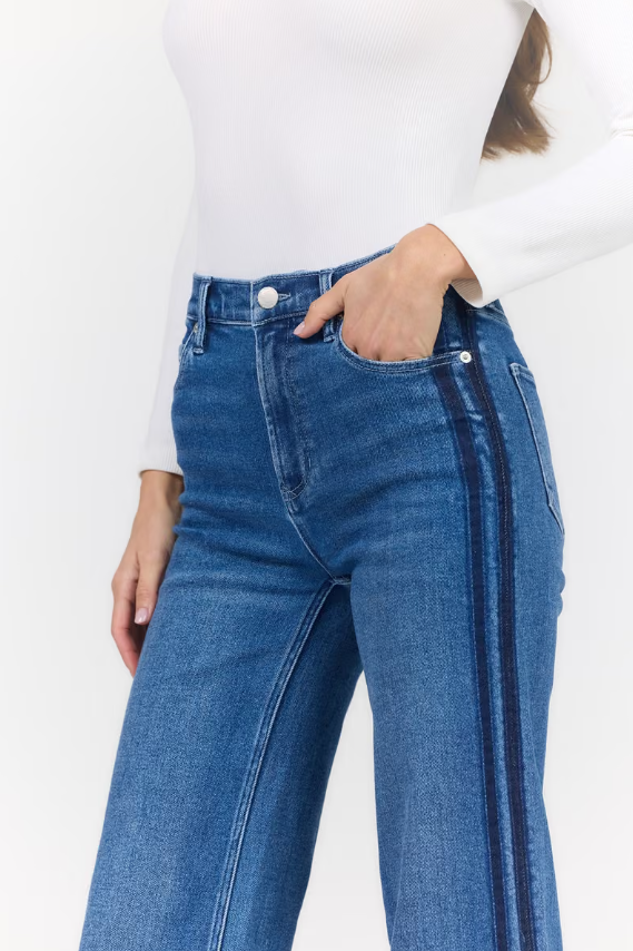A person wearing blue high-waisted wide-leg jeans with dark side stripes, paired with a white long-sleeve top, shown against a plain white background.
