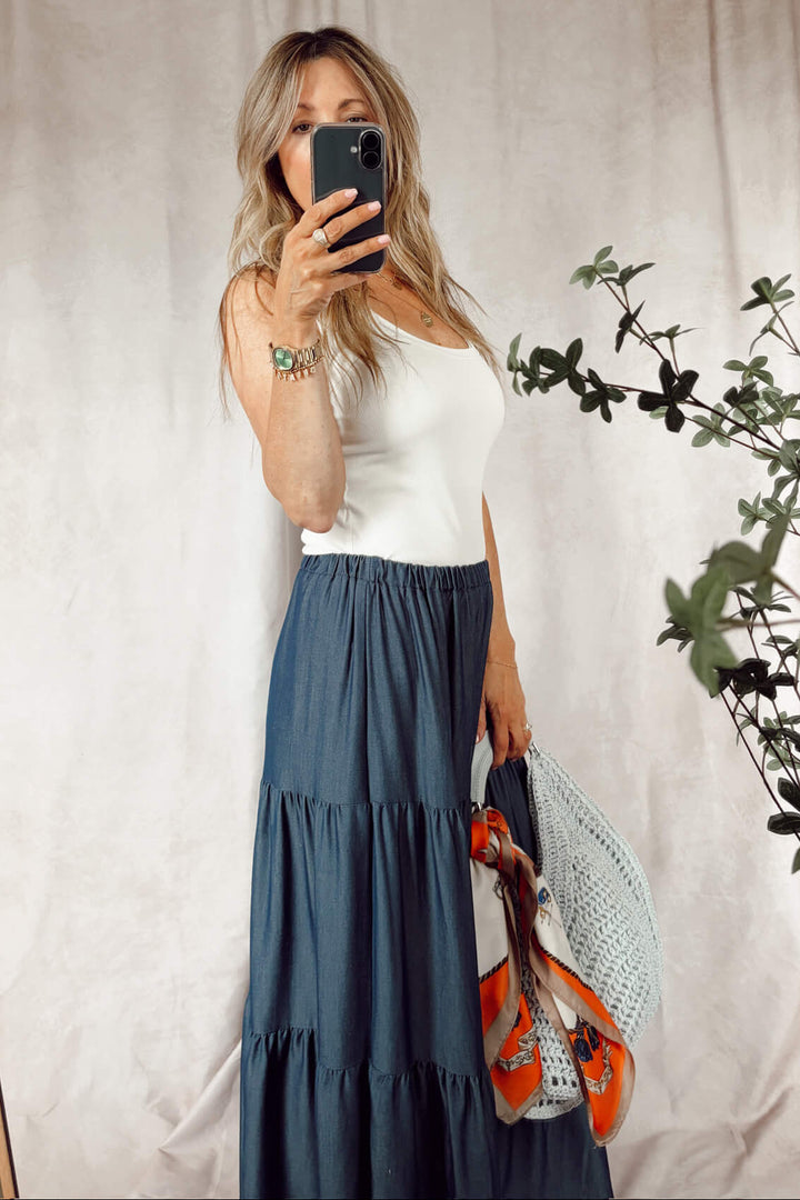 Stanton dark denim tiered maxi skirt with a white tank top and ice blue woven hobo bag with an orange scarf tied around the handle
