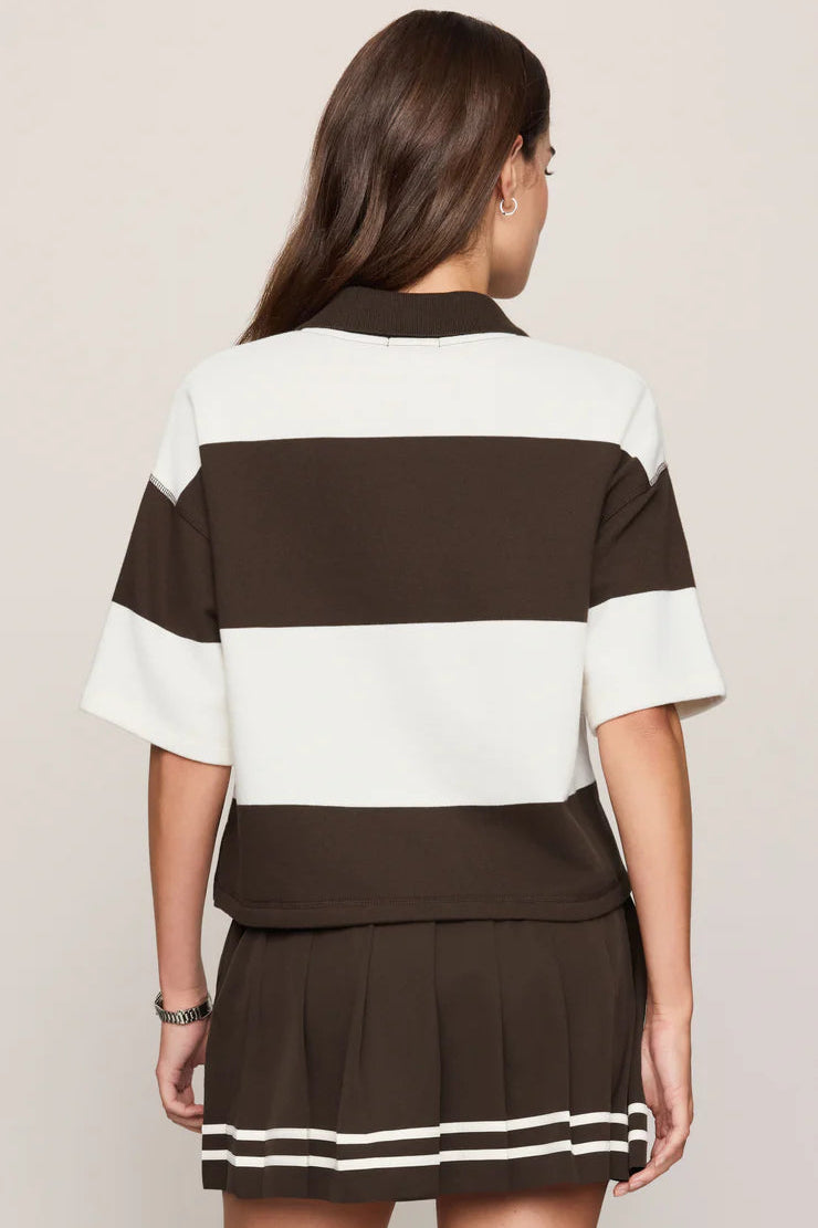 A woman shown from the back wearing a color-blocked short-sleeve top and pleated mini skirt set. The set features horizontal stripes in dark brown and off-white, with matching striped trim on the hem of the skirt.