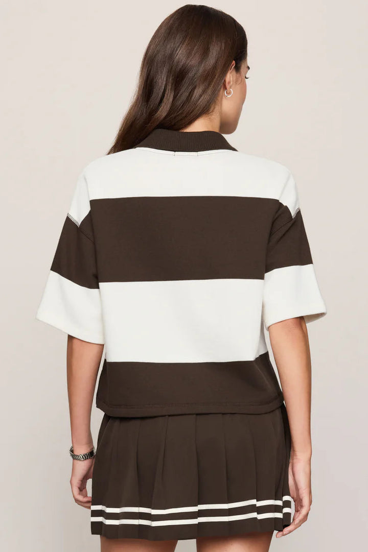 A woman shown from the back wearing a color-blocked short-sleeve top and pleated mini skirt set. The set features horizontal stripes in dark brown and off-white, with matching striped trim on the hem of the skirt.