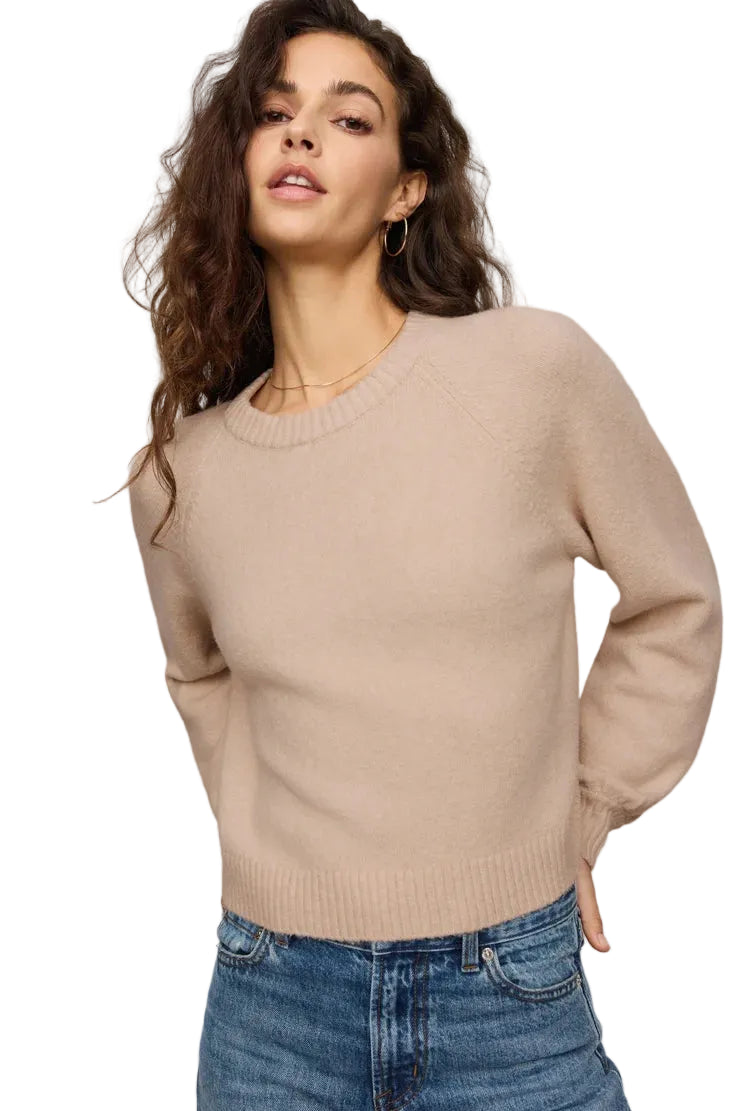 Woman wearing a z supply beige sweater and blue jeans against a plain background