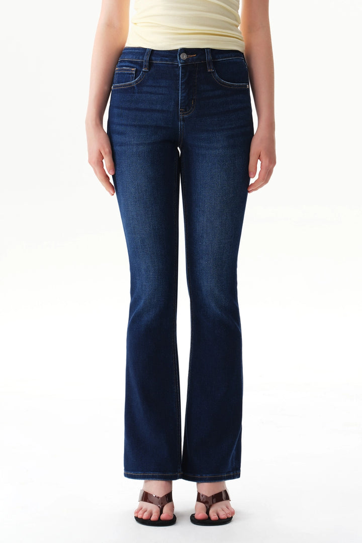 A person wearing dark blue straight-leg  bootcut jeans with a light yellow top and brown sandals, shown from the waist down against a plain white studio background.