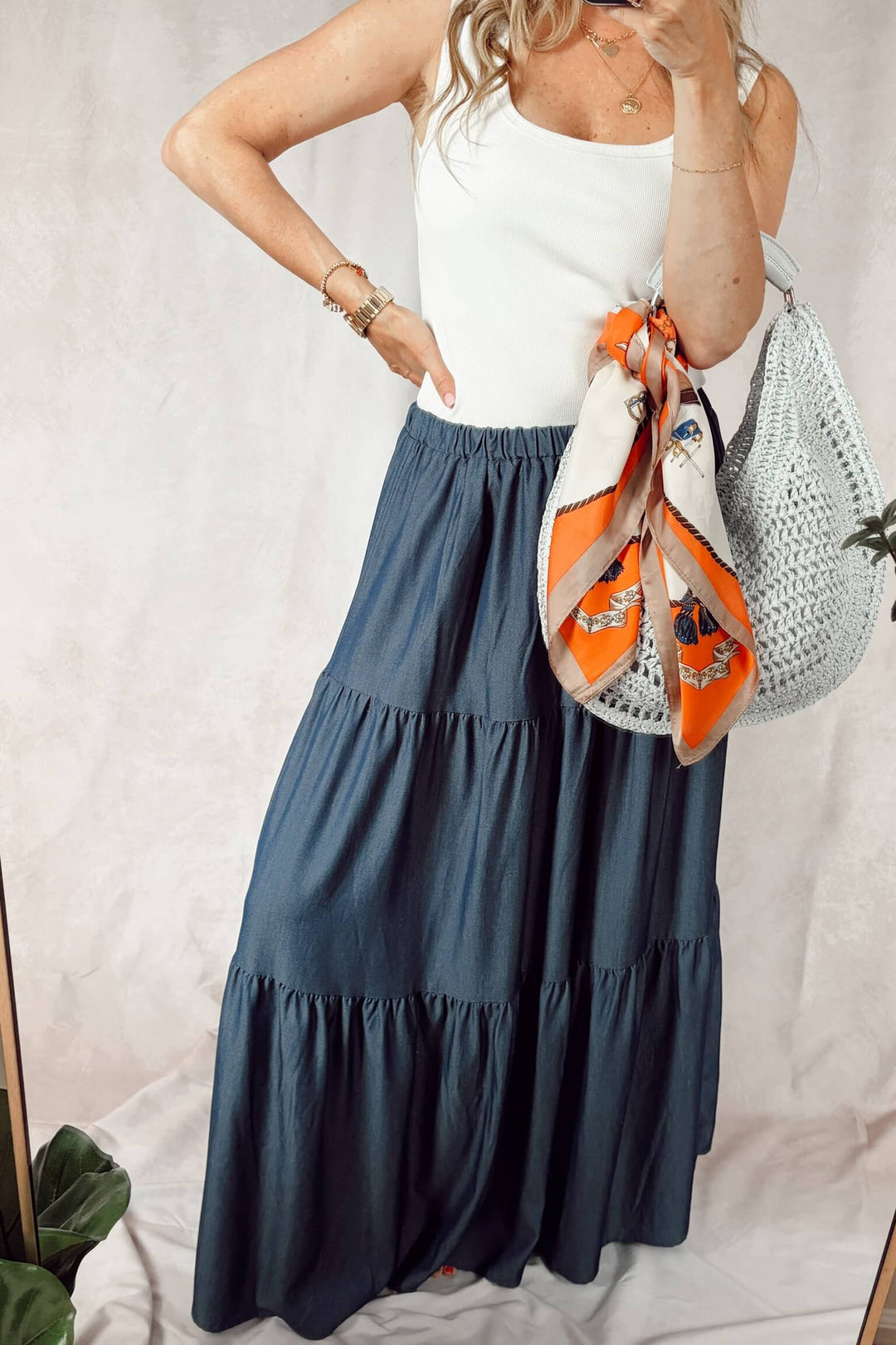 Stanton dark denim tiered maxi skirt with a white tank top and ice blue woven hobo bag with an orange scarf tied around the handle