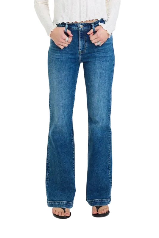 A person wearing medium-wash blue flare jeans with a white ribbed long-sleeve top and black flip-flop sandals, standing against a plain white studio background.