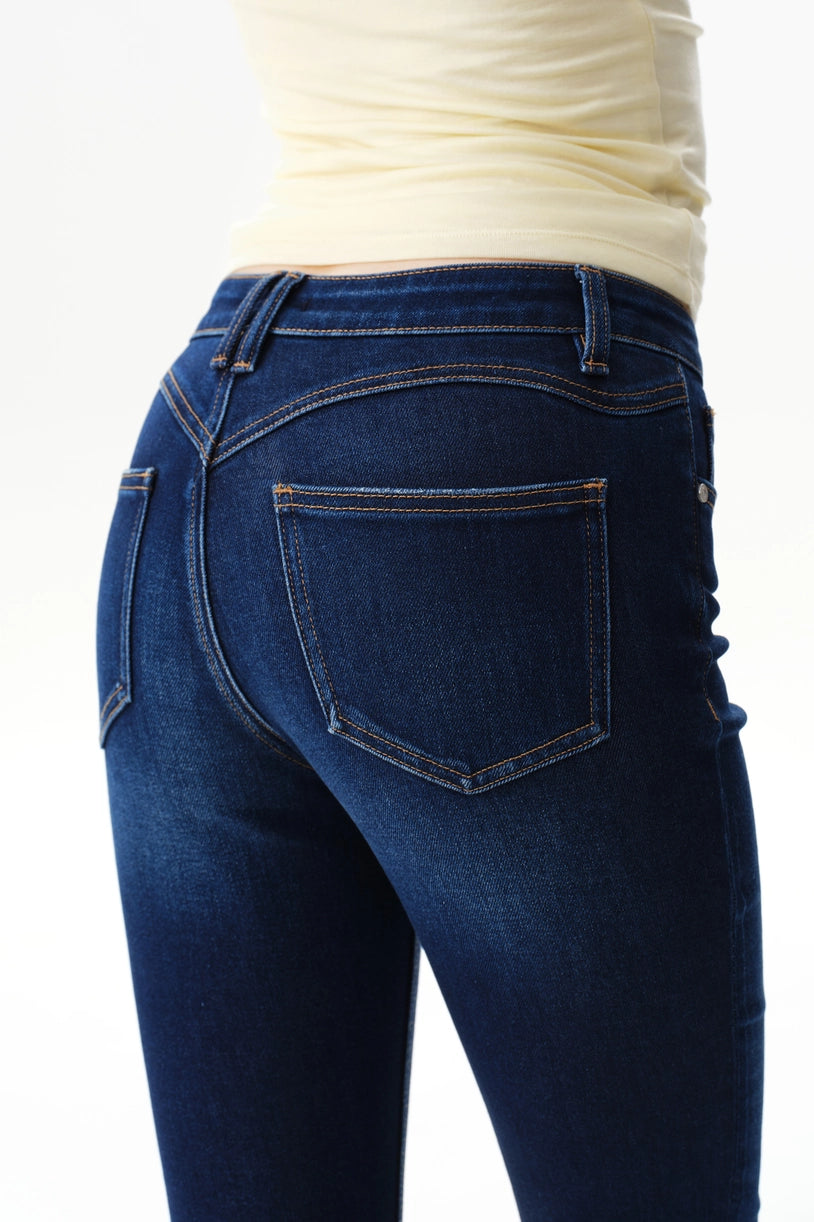 A person wearing dark blue straight-leg  bootcut jeans with a light yellow top and brown sandals, shown from the waist down against a plain white studio background.
