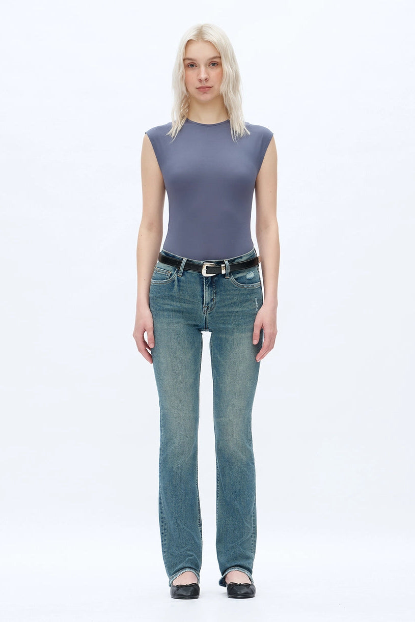 A person wearing dark blue straight-leg  bootcut jeans with a light yellow top and brown sandals, shown from the waist down against a plain white studio background.