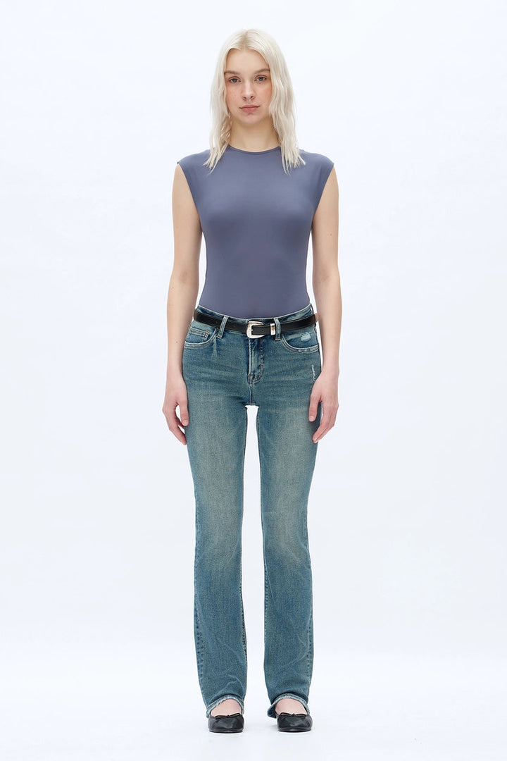 A person wearing dark blue straight-leg  bootcut jeans with a light yellow top and brown sandals, shown from the waist down against a plain white studio background.
