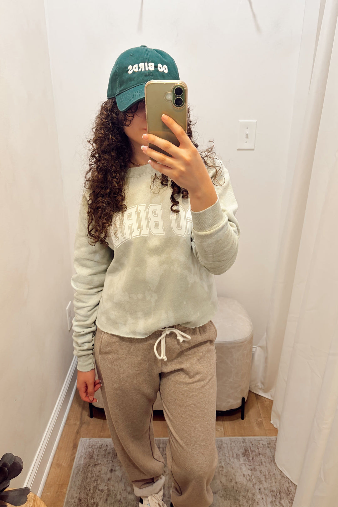 Stanton light sage green tie-dye sweatshirt with white lettering that says Go Birds, beige sweatpants, and a green baseball cap that says Go Birds.