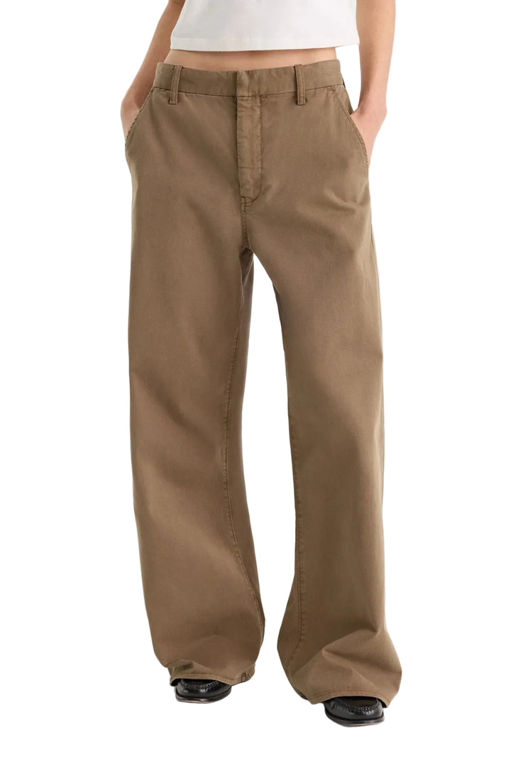 A person wearing wide-leg brown pants with a white cropped top and black shoes, standing against a light gray studio background.