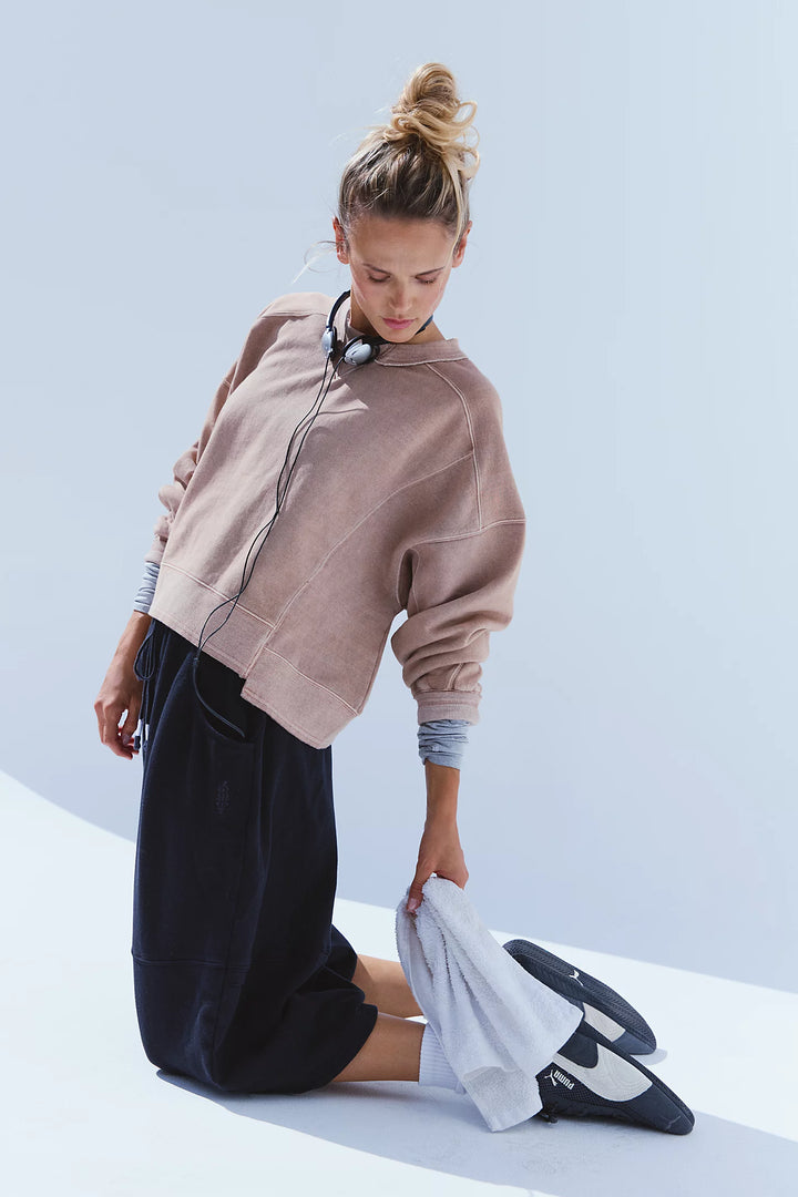 A woman modeling a light brown cropped sweatshirt, black wide-leg shorts, white socks, and dark blue sneakers against a light blue studio background.