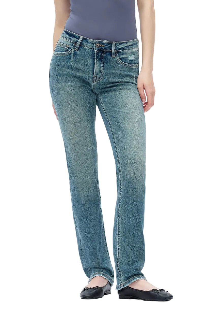 A model wearing a pair of medium-wash blue straight-leg jeans, paired with a slate purple top and black flat shoes, photographed against a seamless white studio background.