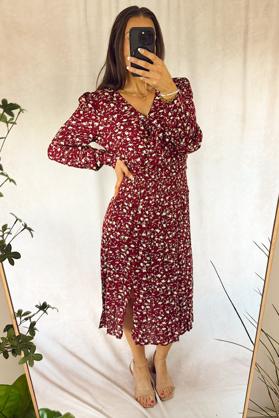 A woman takes a mirror selfie wearing a long-sleeved burgundy midi dress with a white floral pattern. The dress features a V-neckline, puffed shoulders, and a side slit.