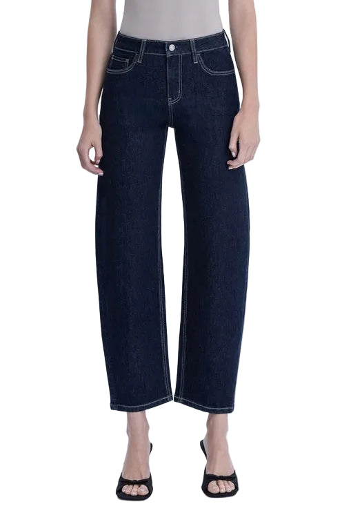 A model wearing dark indigo barrel leg cropped jeans, paired with a light beige top and black strappy sandals, shown against a plain white studio background.