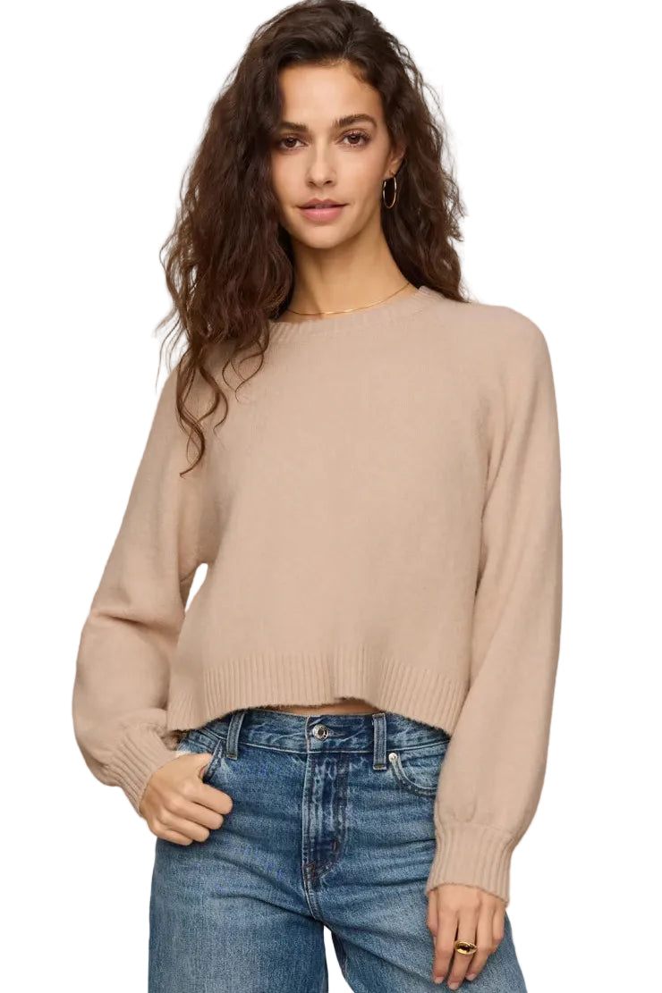 Woman wearing a z supply beige sweater and blue jeans against a plain background